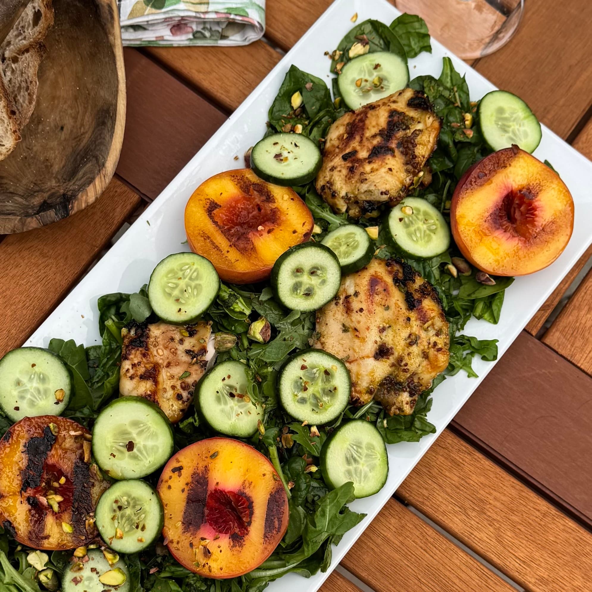 Grilled chicken and peach salad with cucumber, arugula, and pistachios on a white platter
